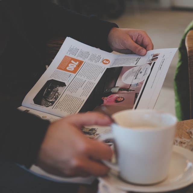 Closeup of a man’s hands holding coffee reading magazine.